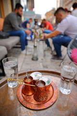 Traditional Bosnian coffee cups (with a copper tray) with young people smoking Shisha (or Hookah) in the background, Sarajevo, Bosnia and Herzegovina
