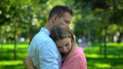 Man hugging and comforting upset girlfriend in park, togetherness and support