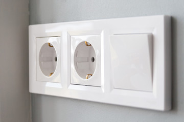 A closeup diagonal view of a group of white european electrical outlets and a switch located on a...