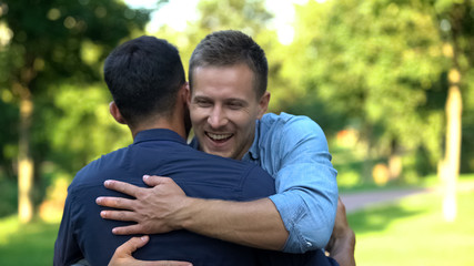Two male friends hugging outdoors, pleasure emotions, friendship happiness
