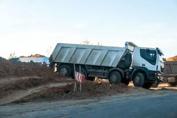 Dirty white dump truck standing on a large pile of ground during road works on an intercity highway