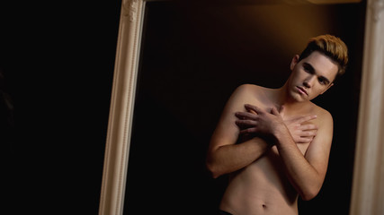 Shy trans man closing naked torso in front of mirror, breast surgery desire - obrazy, fototapety, plakaty