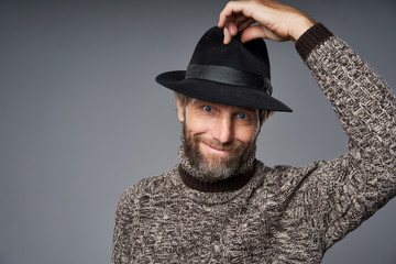 Smiling mature man in warm sweater lifting his hat greeting