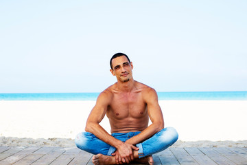 young muscular man in denim pants resting and posing on the beach