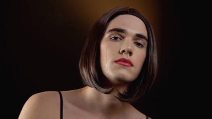 Crying agender in wig with makeup looking at cam, victim of social condemnation