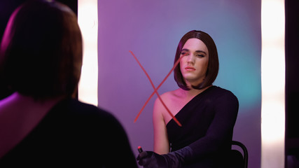 Trans man holding lipstick looking in mirror with cross sign, identity disorder