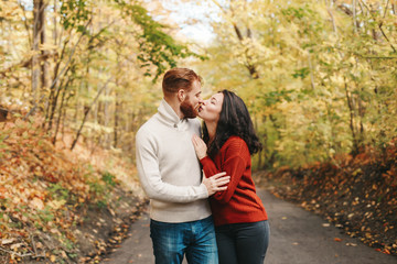 Portrait of beautiful couple man woman in love. Boyfriend and girlfriend hugging kissing outdoor in park on autumn fall day. Togetherness and happiness. Authentic real people feelings.