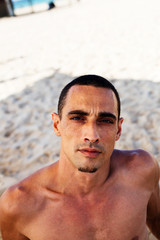 young muscular man in denim pants resting and posing on the beach