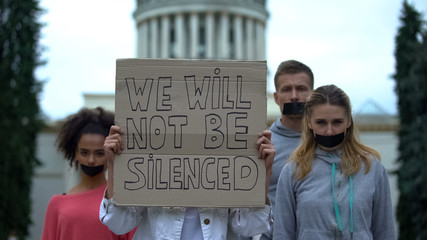 Young people with taped mouth showing banner against concealment of crime, abuse