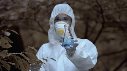 Female scientist showing test tube radioactive water marked poison, biohazard