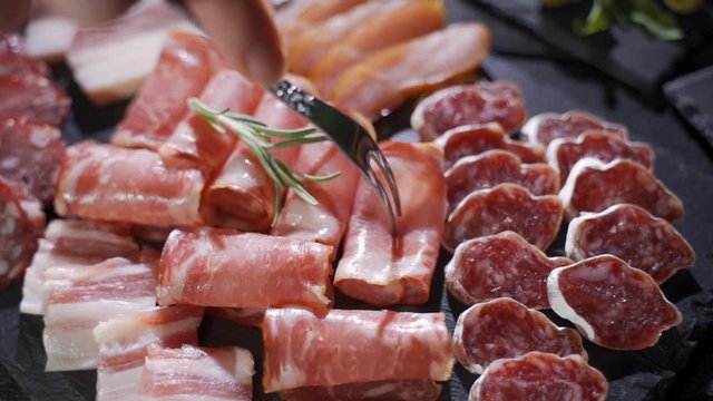 Assorted deli meats, ham, salami, bacon and tomatoes on the black stone tray