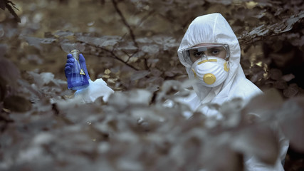 Female biologist in protective uniform holding infected water sample, poisoning