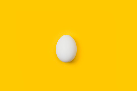 Un huevo blanco de gallina sobre fondo amarillo brillante liso y aislado. Vista superior y de cerca. Copy space