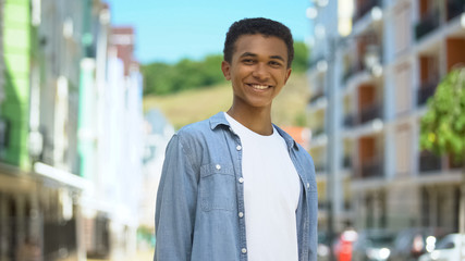 Inspired mixed-race male millennial smiling at camera on city street, future