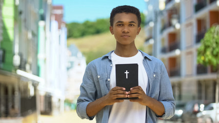 Teen male christian holding holy bible near heart, faith and belief, religion