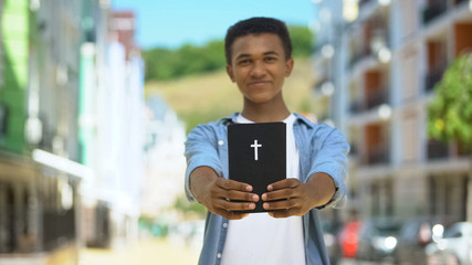 Happy african-american boy showing holy bible on camera and smiling, religion