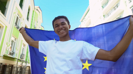 Cheery mixed-race young man holding European Union flag outdoor, freedom march