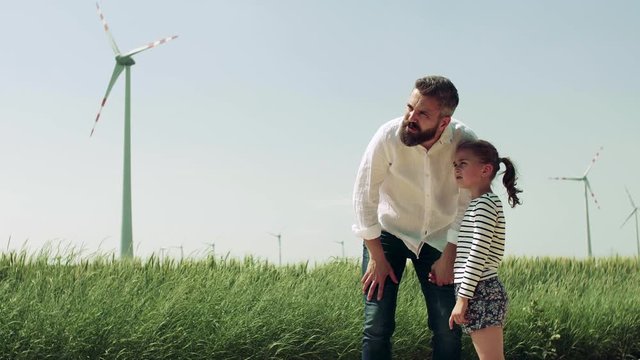 Mature father with small daughter on field on wind farm, talking.