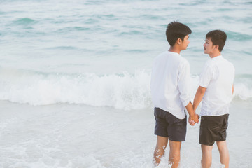 Back view homosexual asian couple standing together on beach in summer, asia gay holding hands going sea for leisure and relax with romantic and happy in vacation at sea, LGBT with legal concept.