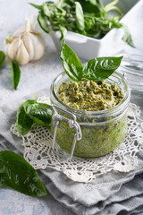traditional italian basil pesto sauce in a glass jar on a light stone table