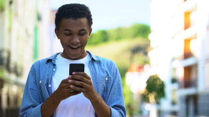 Excited teenager smiling reading message about sales and discounts on smartphone