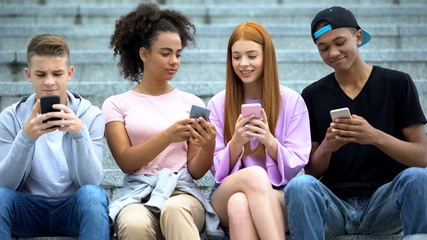 Group of college students playing smartphone game sitting outdoor stairs, gadget