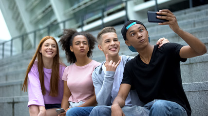 Carefree young people posing for smartphone selfie sitting outdoors, friendship