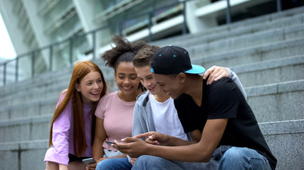 Happy university students watching online video by smartphone having fun, gadget