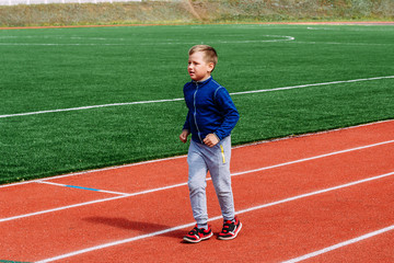 Fototapeta premium eight-year-old Caucasian boy in red sneakers runs through a sports stadium