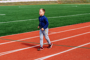 Fototapeta premium ośmioletni kaukaski chłopiec w sportowym mundurze biegnie na czerwonej bieżni stadionu