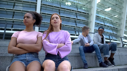 Obraz premium Two male teenagers laughing at female classmates sitting beside, youth gossips