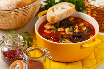 Traditional Spanish goulash soup. Fabada Asturiana. Served with a yellow clay pot with lid. Front...