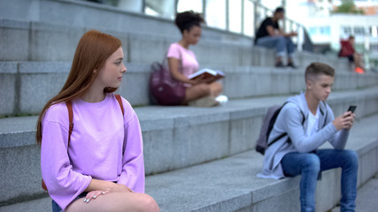 Lonely teenager girl suffering from unrequited love looking at male classmate