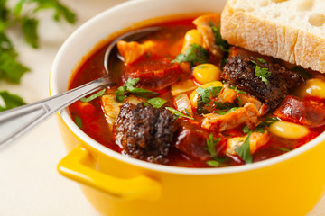 Traditional Spanish goulash soup. Fabada Asturiana. Served with a yellow clay pot with lid. Front...