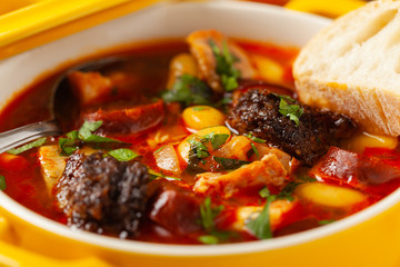 Traditional Spanish goulash soup. Fabada Asturiana. Served with a yellow clay pot with lid. Front view.