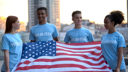 Joyful multiethnic volunteers holding American flag, charity project, support