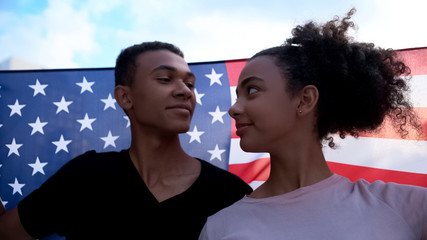 Cheerful multiracial students in love holding USA flag looking each other, march