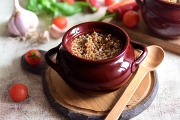 Buckwheat with meat in a clay pot for baking on a wooden Board. Buckwheat porridge with meat and onions in a baking dish