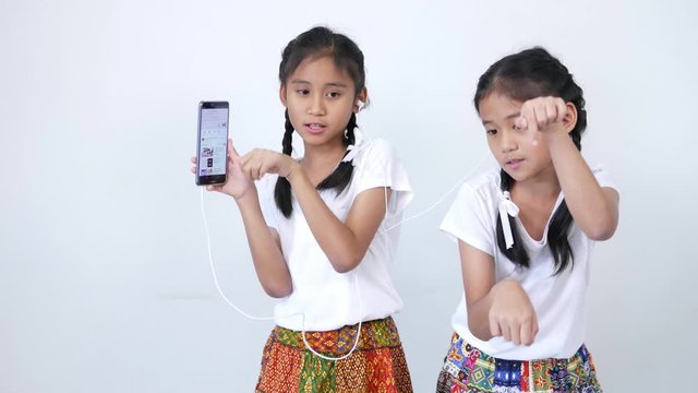 Two girl wore the white shirt, braid and tied lovely white ribbon, listening to music on smartphone with phone headset, enjoying and singing softly, follow the music and dance slowly.