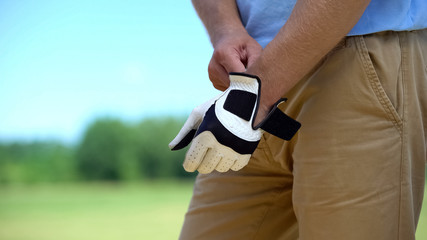 Male golfer wearing qualitative white glove, preparing to play, elite hobby