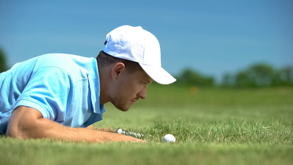 Male golf player looking at ball rolling in hole at course, hoping for goal