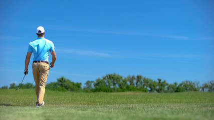 Athletic man with iron club walking on course, sport and training, elite hobby