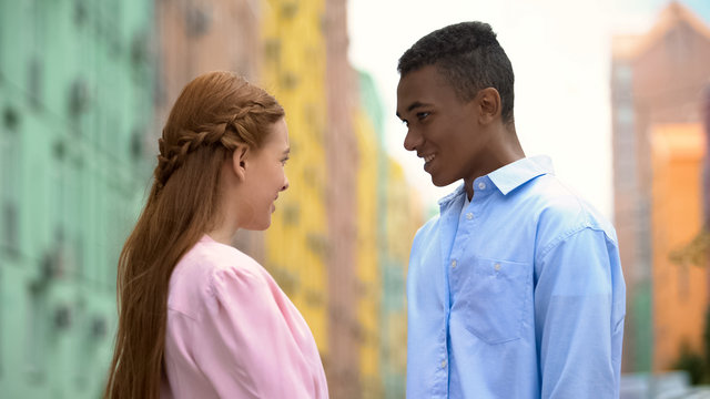 Smiling couple of teenagers looking at each other, meeting in city center, date