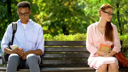 Shy teens sitting on different parts of bench, hesitating to tell about feelings