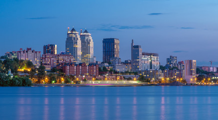 Fototapeta premium Panoramic view of the towers, skyscrapers, promenade in the evening, the lights are reflected on the Dnieper River, Ukraine. Dnipro city, Dnipropetrovsk.