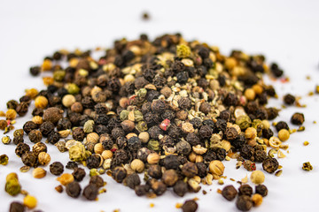 Pile of different types of peppercorns to season cooking recipes over white background
