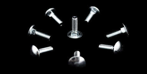 A lot of shiny metallic screws on black background arranged in a circular and concentric shape