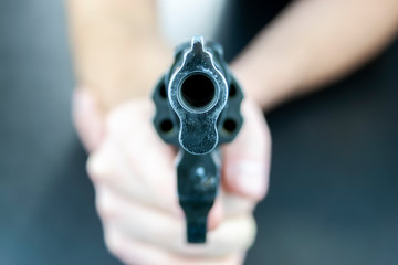 A hand is holding a revolver, with barrel facing the camera. Camera is focused on the barrel of the revolver