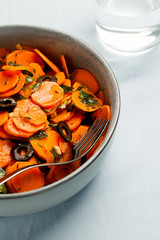 Traditional Moroccan cooked carrot salad North African vegan dish with chopped parsley and olives on gray plate close-up copy space.Healthy organic food for holiday dinner.Vertical orientation