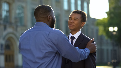 Joyful parent hugging graduating son in suit outdoors academy, prom celebration © motortion